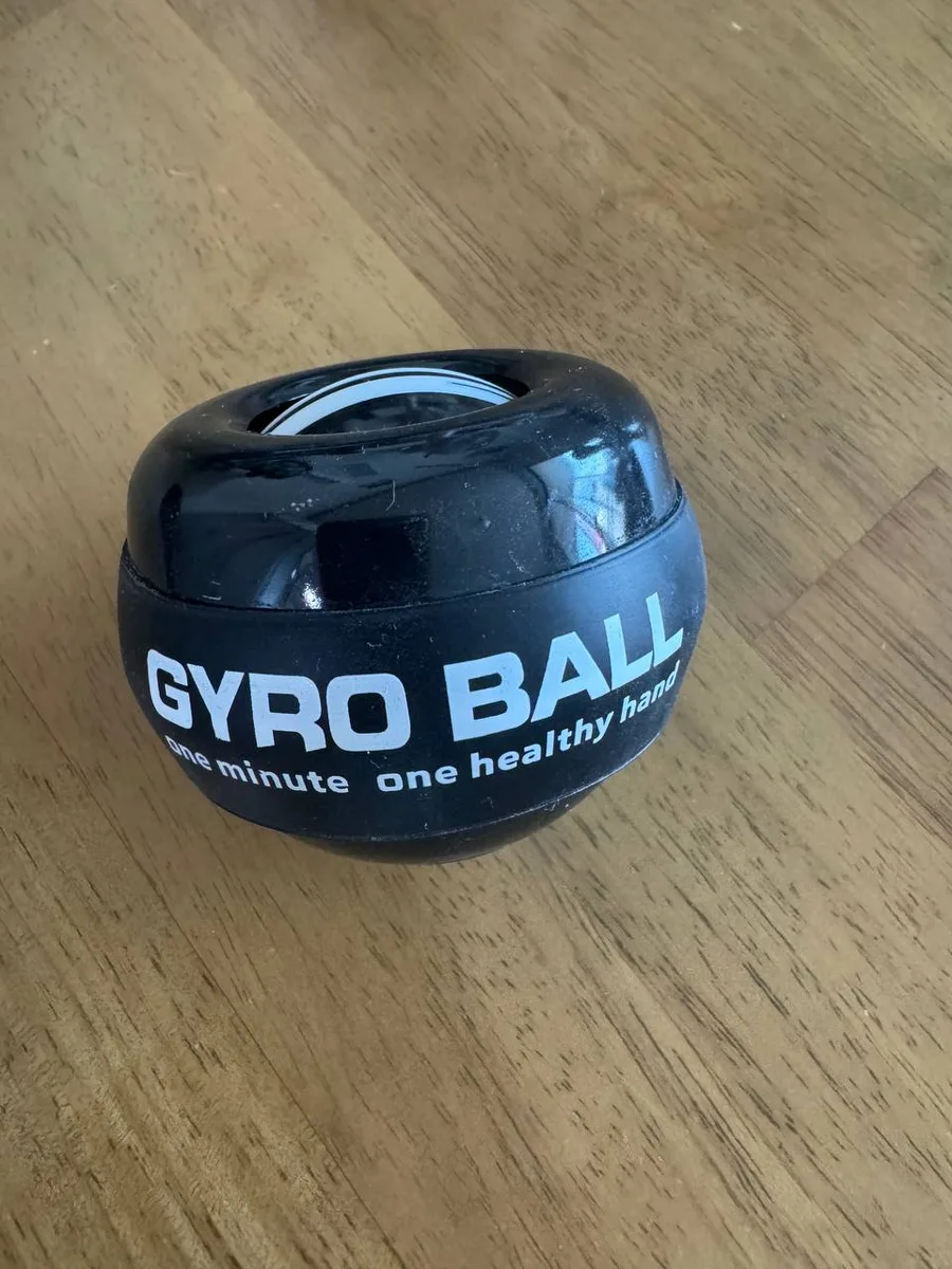 나무 책상 위에 놓인 검은색 자이로볼. 겉면에 GYRO BALL 문구가 인쇄된 고무 밴드가 감겨 있다