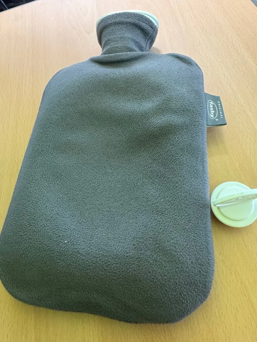 회색 플리스 커버를 씌운 파쉬 보온 물주머니가 책상 위에 놓여 있고, 옆에 연두색 마개가 분리되어 있다